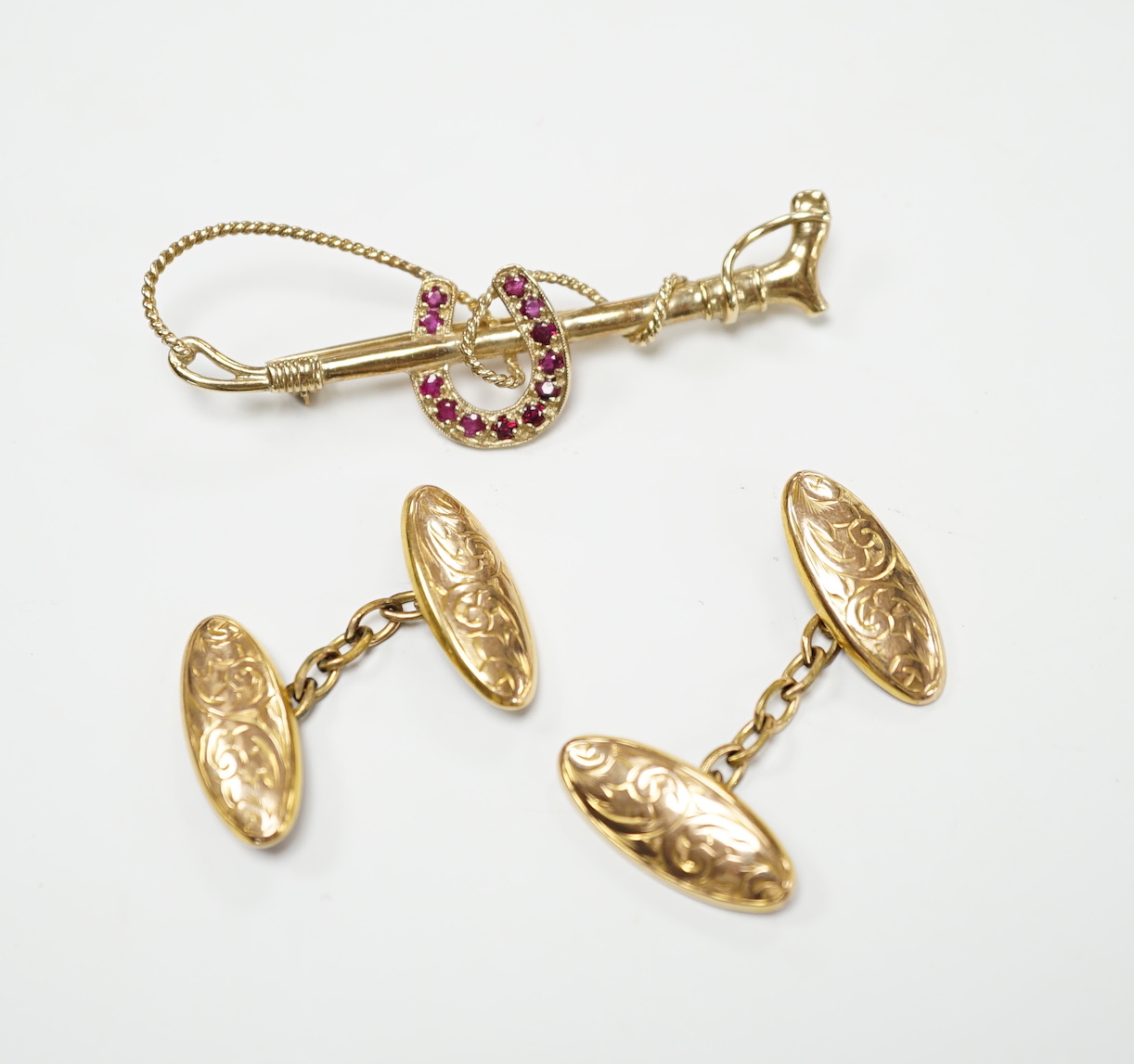 A pair of George V engraved 9ct gold oval cufflinks and a yellow metal and ruby cluster set horseshoe and riding crop bar brooch, gross weight 7.1 grams.